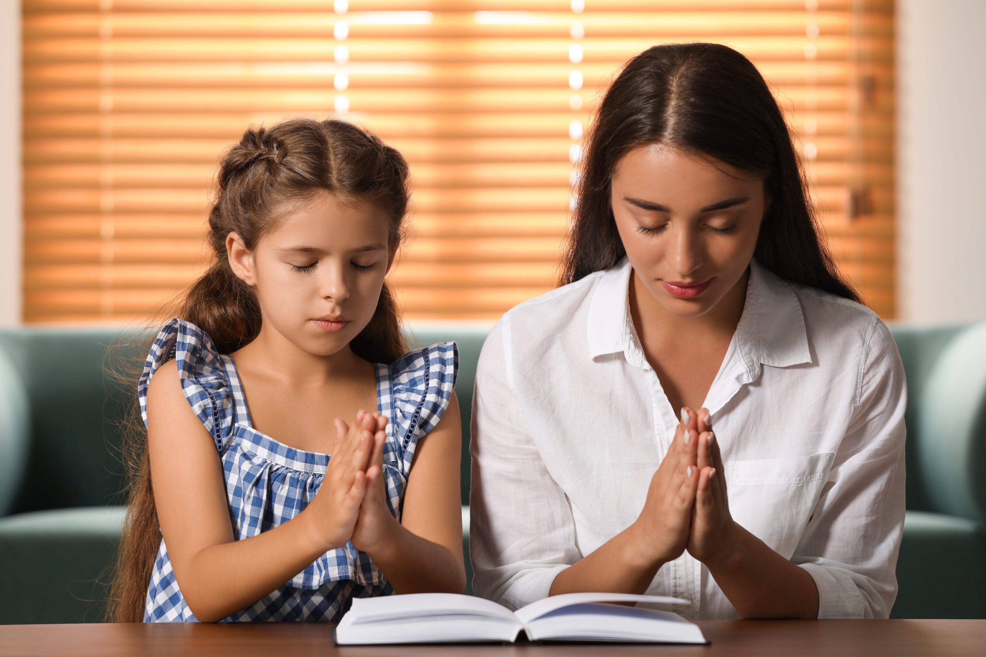 Child and woman praying with open book.
