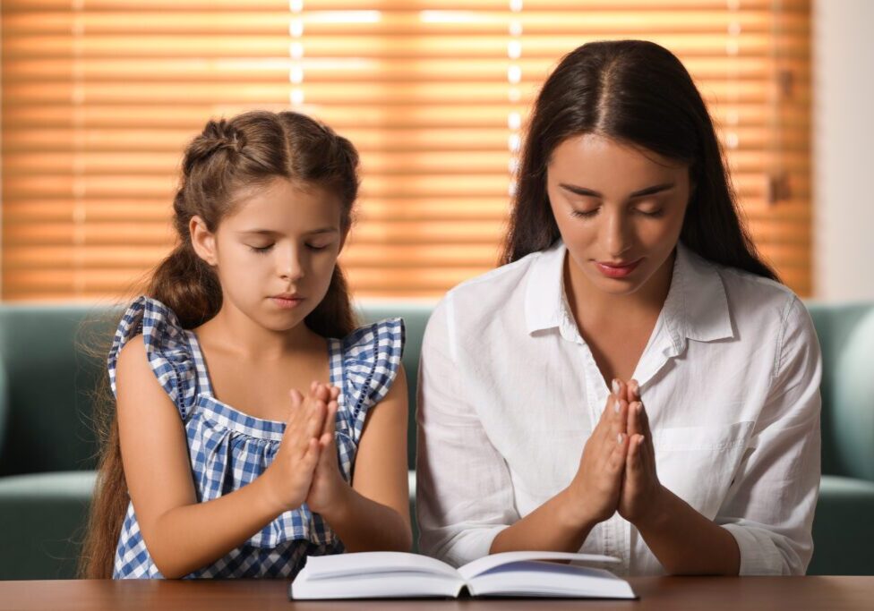 Child and woman praying with open book.