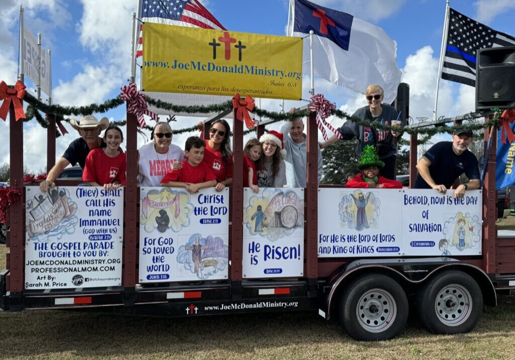IMG_0285 People on a decorated trailer holding signs and flags during a parade.